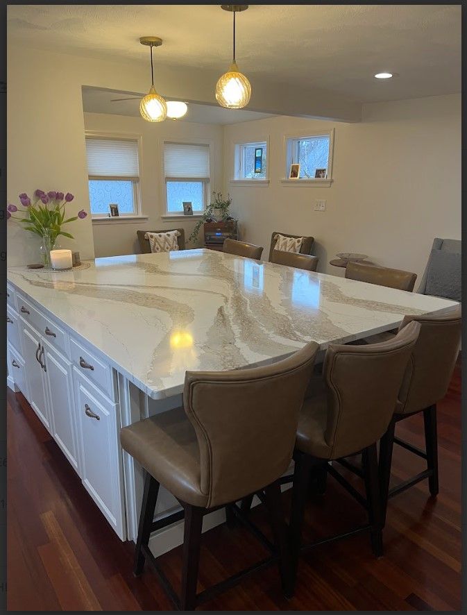 Kitchen island with white cabinets, marble countertop, and brown leather bar stools under pendant lights.