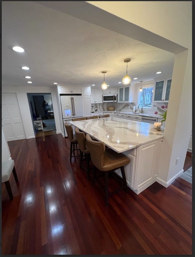 Spacious kitchen with a large island, hardwood floors, white cabinets, and pendant lights.