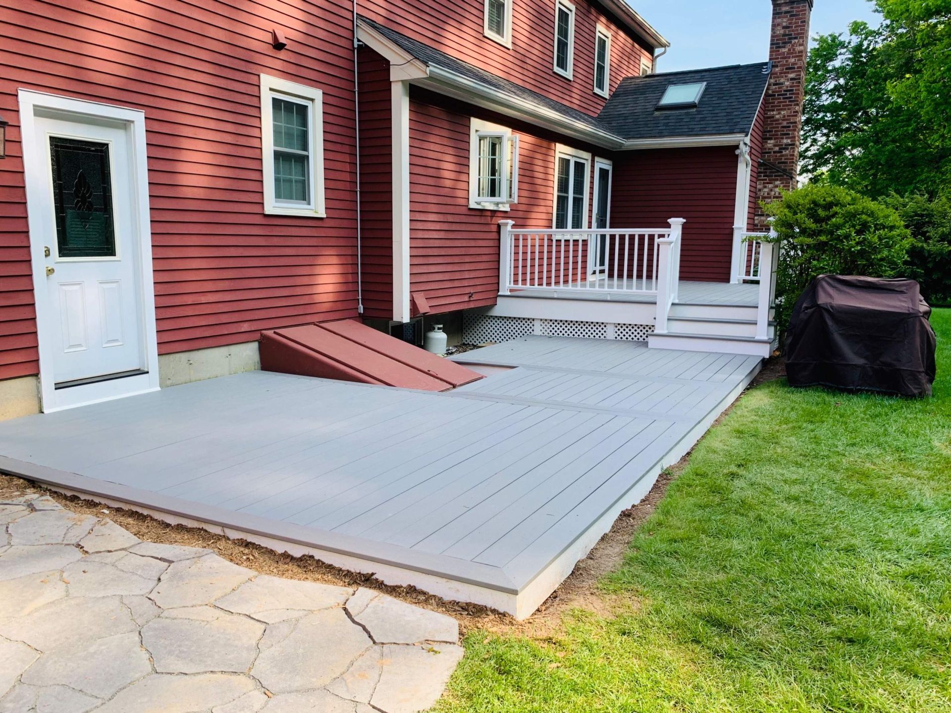 Red house with gray deck, steps, and ramp. A grill sits nearby on the grass.