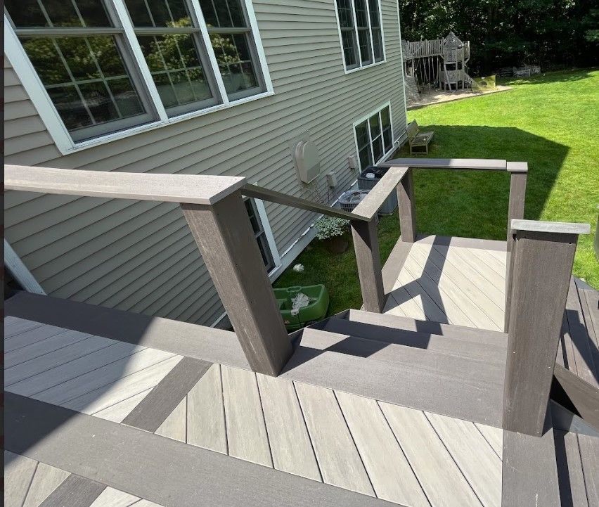 Deck with steps, railing, and house. Gray composite deck and siding. Sunny day.