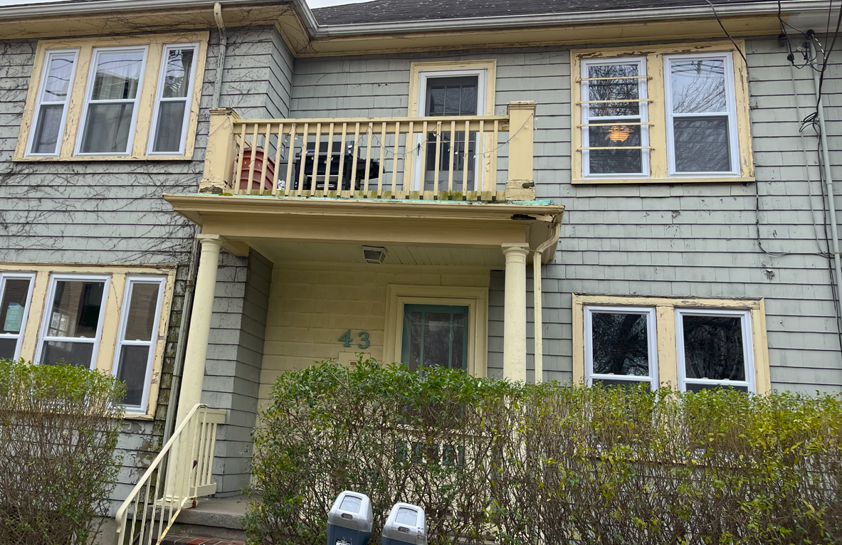 Dilapidated light green building with porch, balcony, and beige trim.