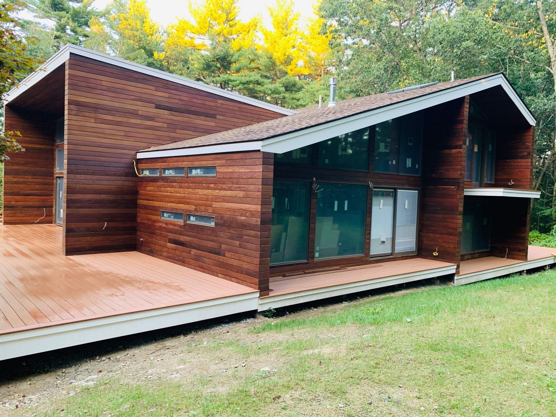 Wood-sided house with large windows, an attached deck, and a backdrop of trees.