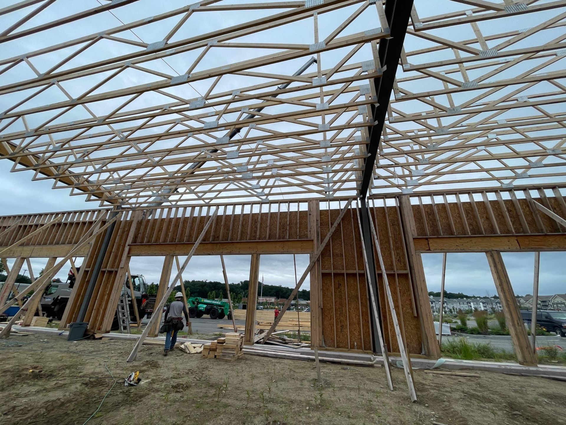 Construction site: Wooden framing, roof trusses, workers. Cloudy sky background.