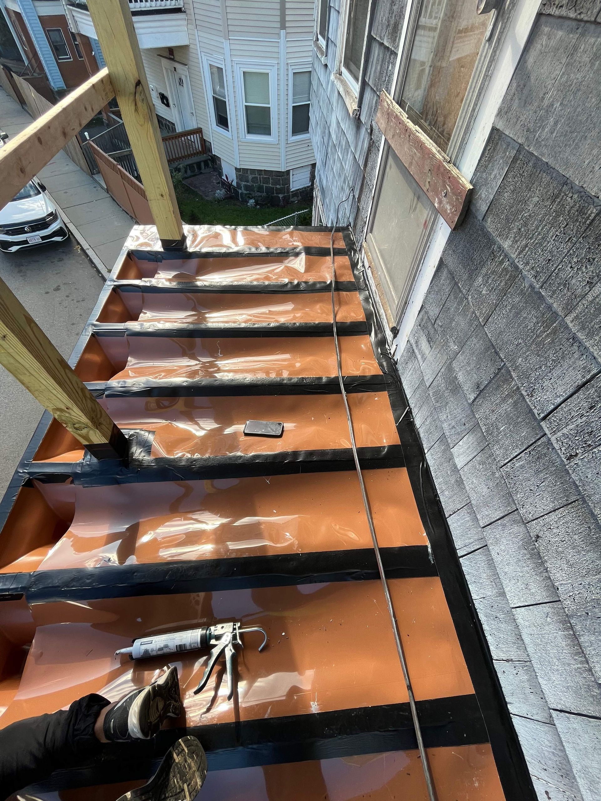 Overhead view of a rooftop stairwell. Orange roofing material with black trim. Wooden scaffolding is present.