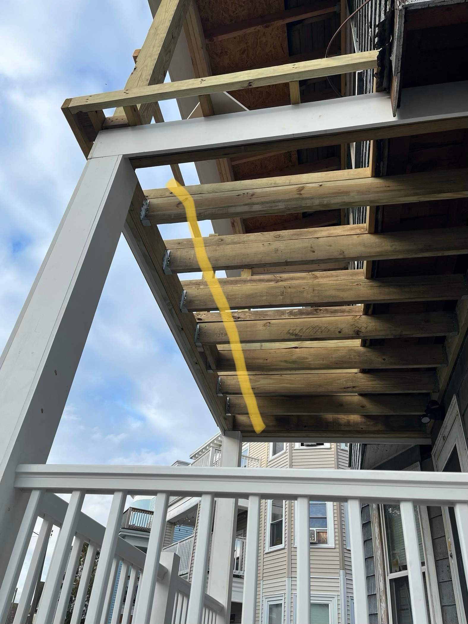 View of a deck's underside with wooden planks and white railing. A yellow line highlights a plank.