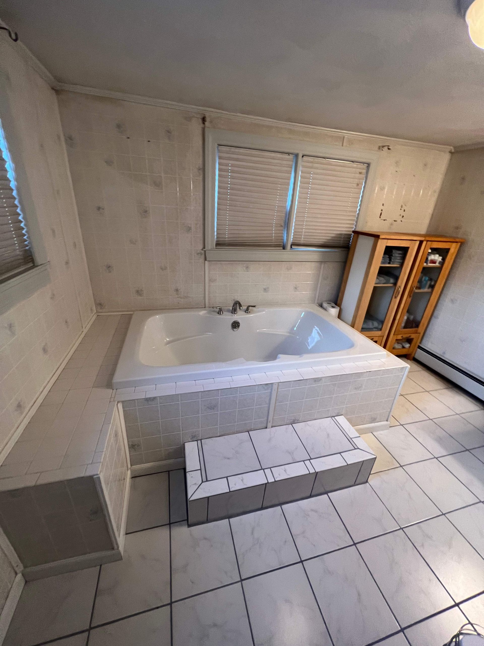Bathroom with a built-in white jacuzzi tub, tile floor, and a cabinet.