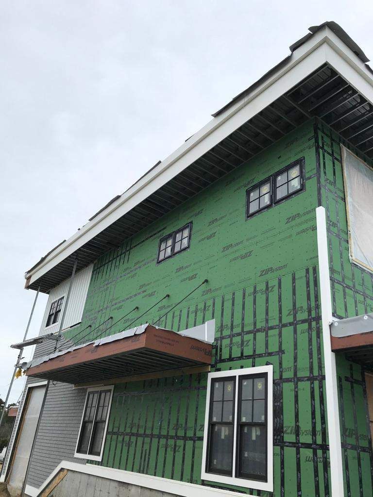 Green house exterior under construction, black windows, gray siding, white trim, cloudy sky.