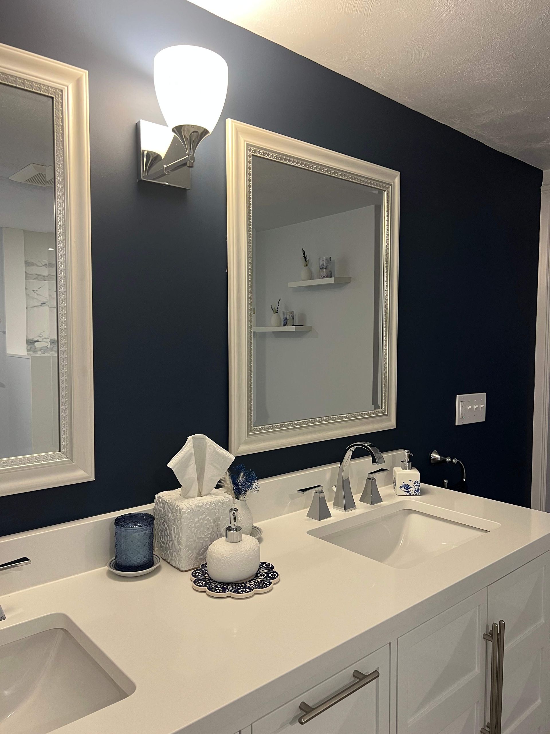 Bathroom with white vanity, blue wall, two mirrors, and a sconce light.