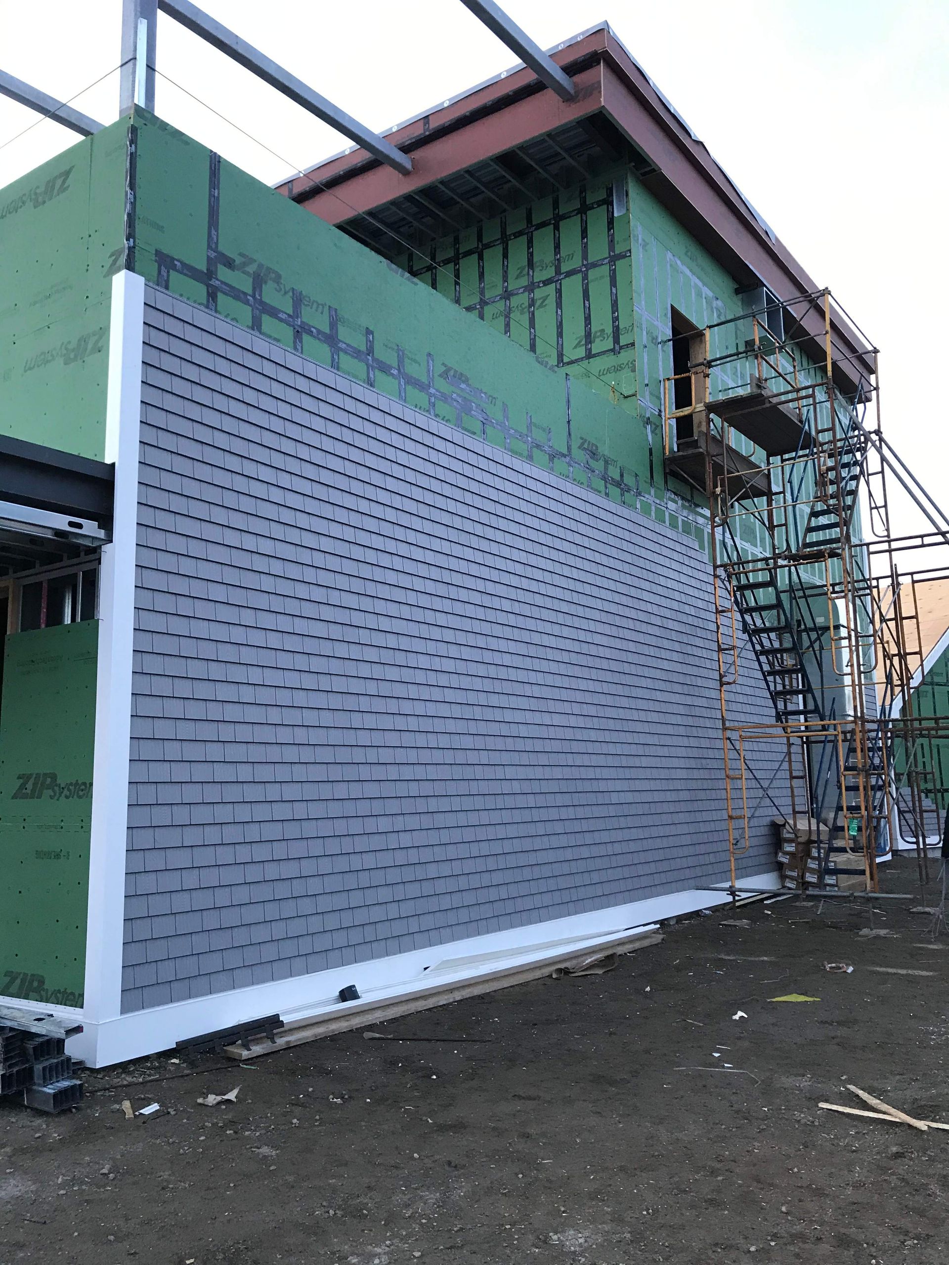 Building under construction; gray brick facade being installed on exterior wall. Scaffolding is visible.