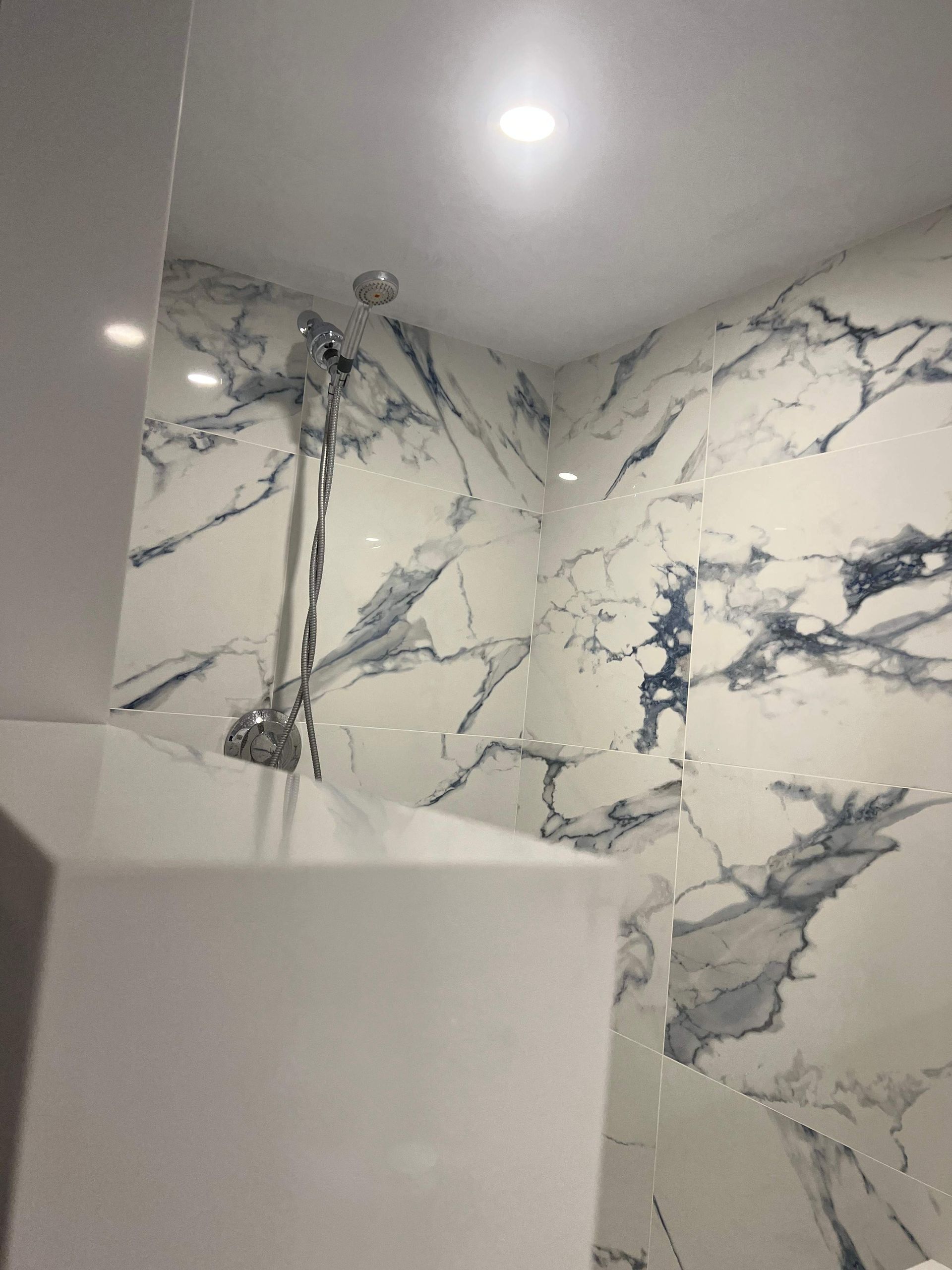 Shower with marble-look tile walls, chrome fixtures, and a recessed ceiling light.