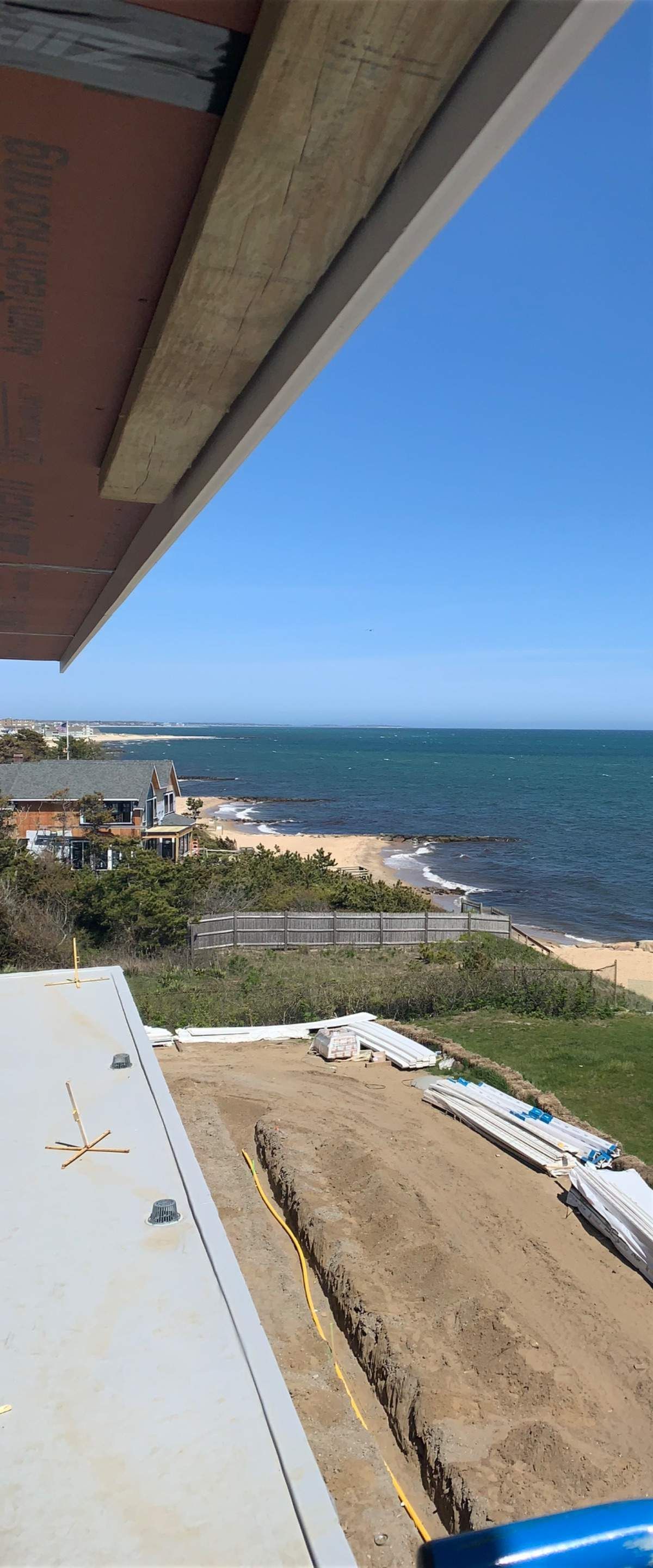 View of the ocean from a building under construction. Sunny, blue sky. Beach and houses in the distance.
