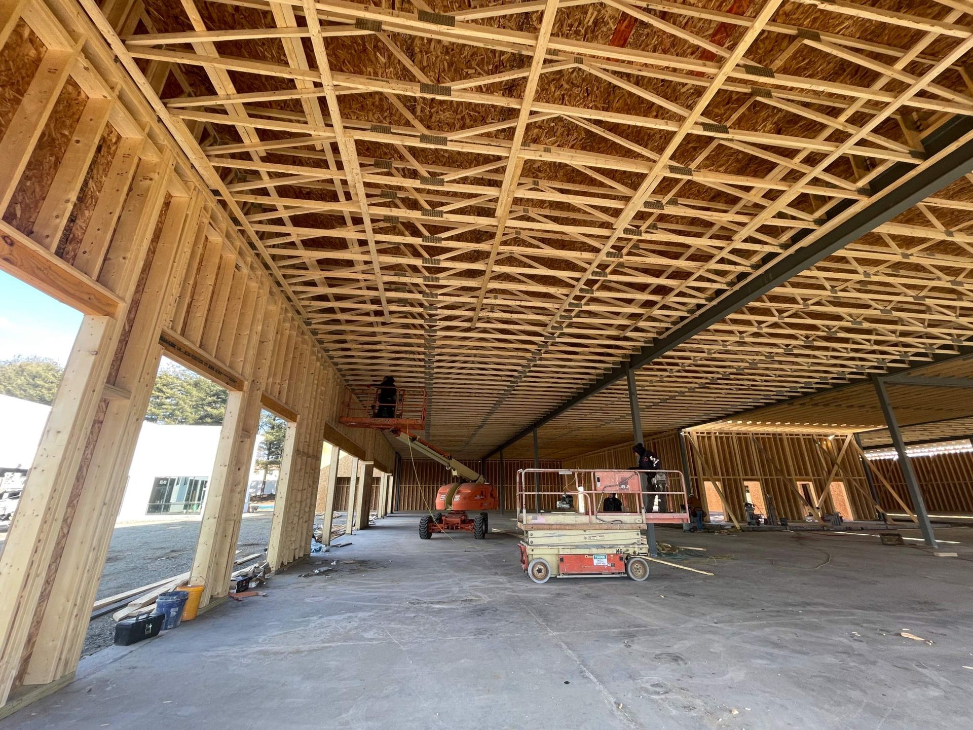 Interior of a building under construction, showing wooden framing, beams, and scissor lifts.