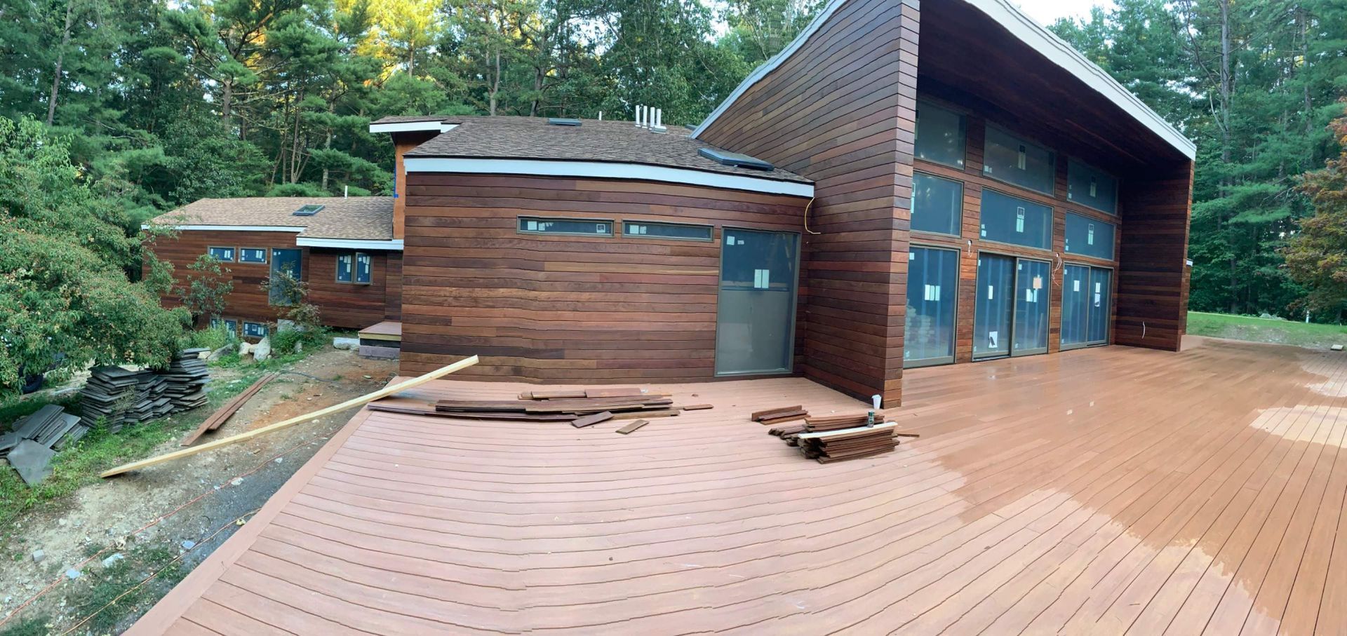 Exterior of a dark wood-clad building with a large deck in a wooded setting.