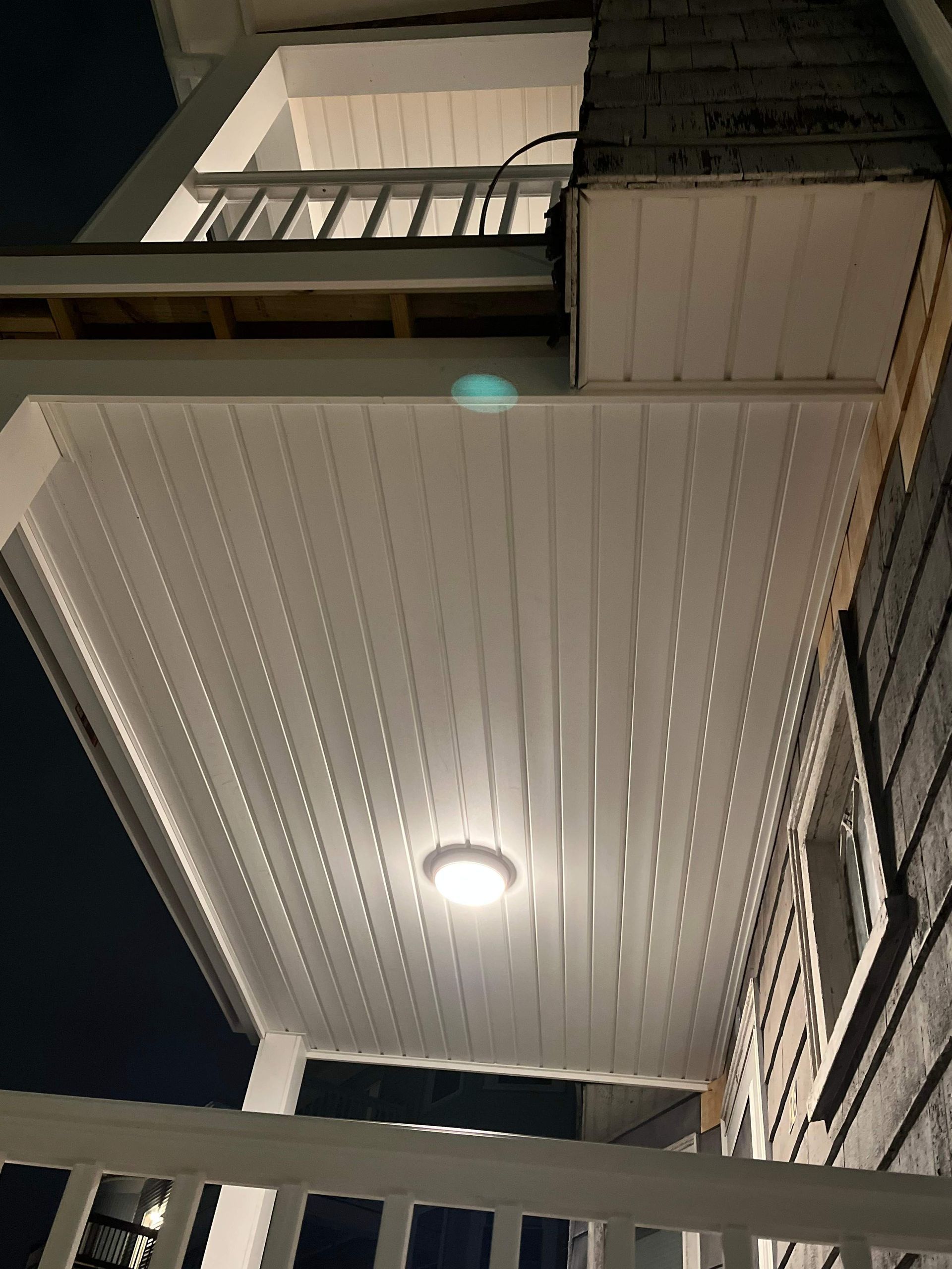 White porch ceiling with a centered light fixture and a second-story balcony with a railing.