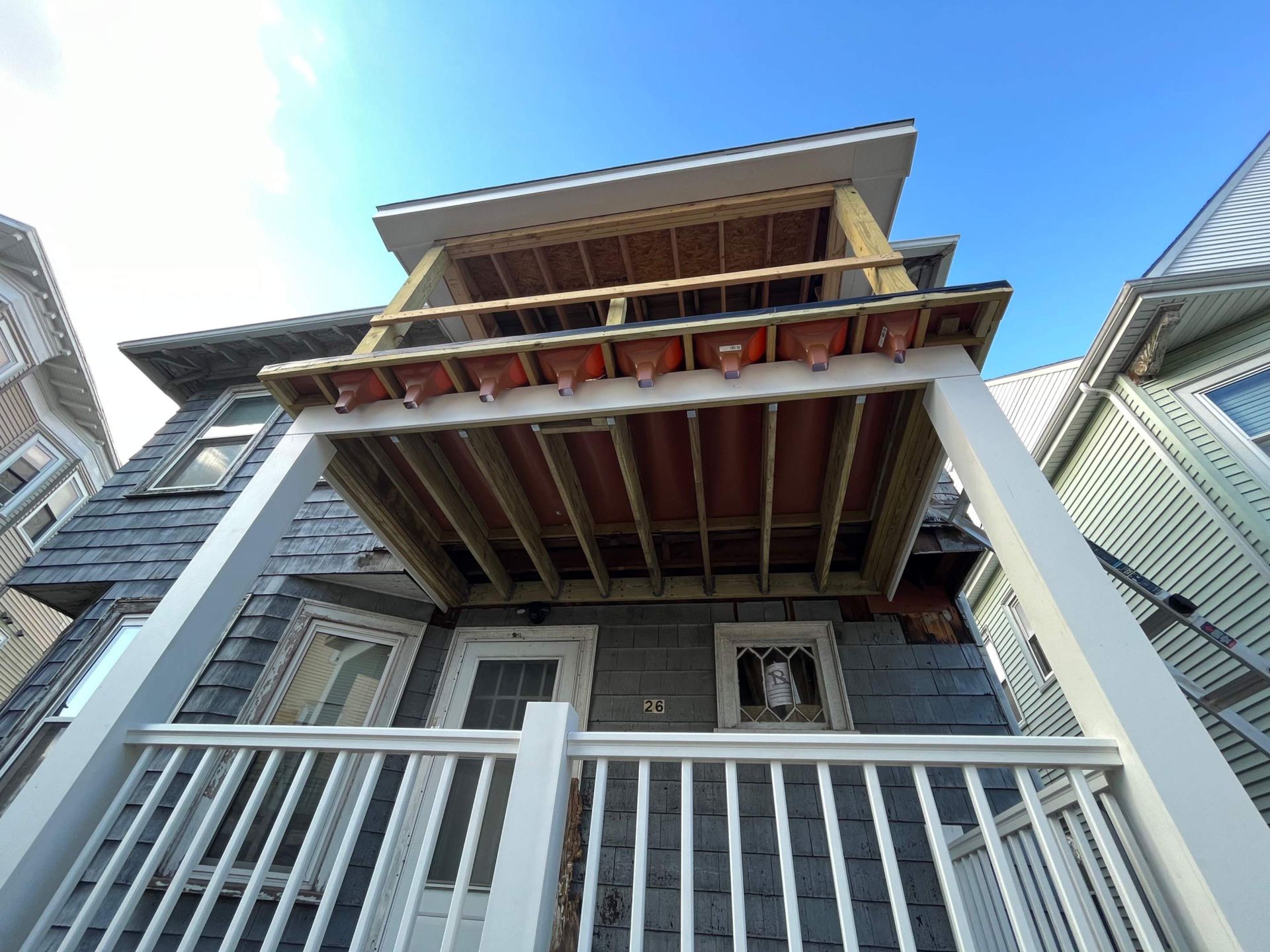 Low-angle view of a two-story wooden porch addition on a gray house, against a blue sky.