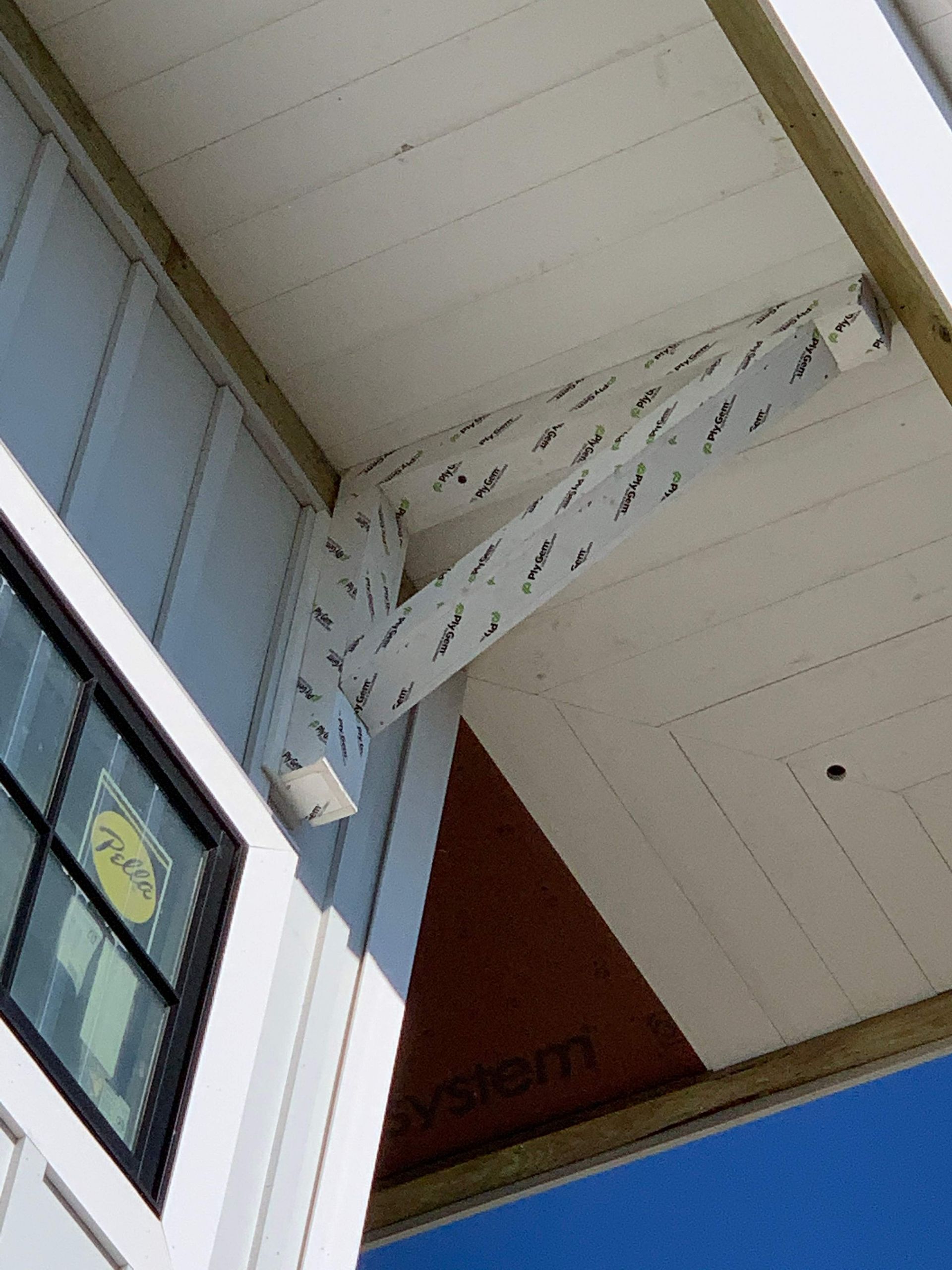 Corner of a building with white siding, black window, and a wrapped structural support beam.