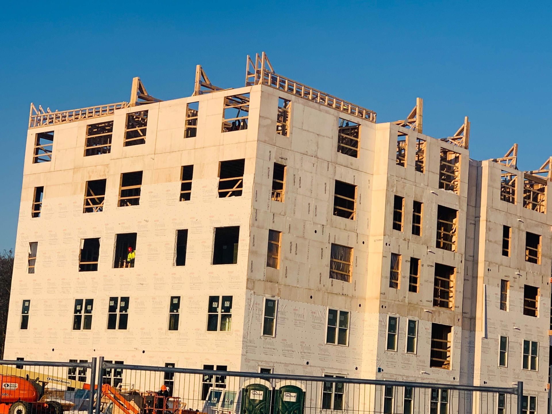 Construction of a multi-story wood-framed building with numerous window openings against a blue sky.