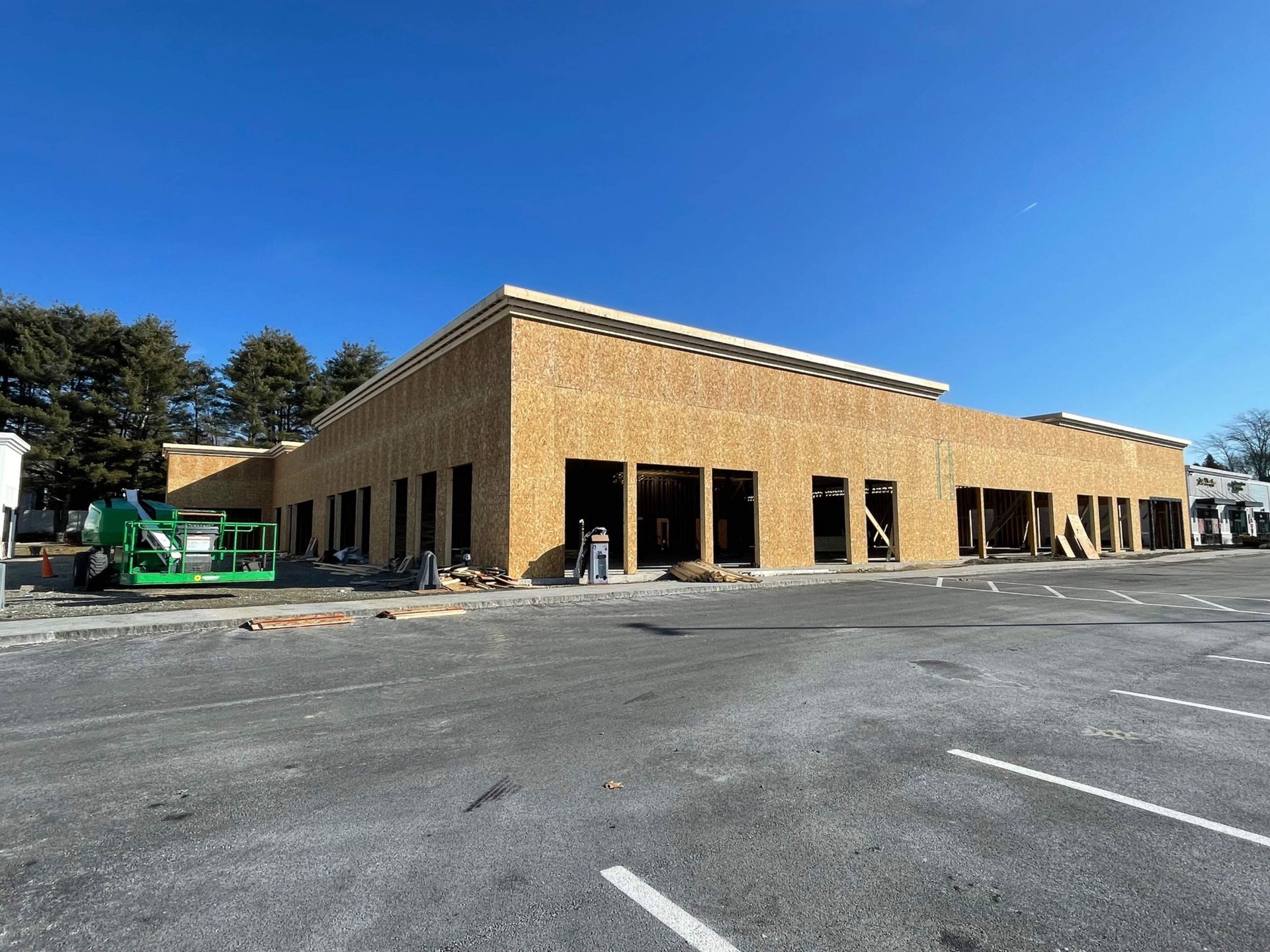 Building under construction, brown wood exterior, black window frames, parking lot.