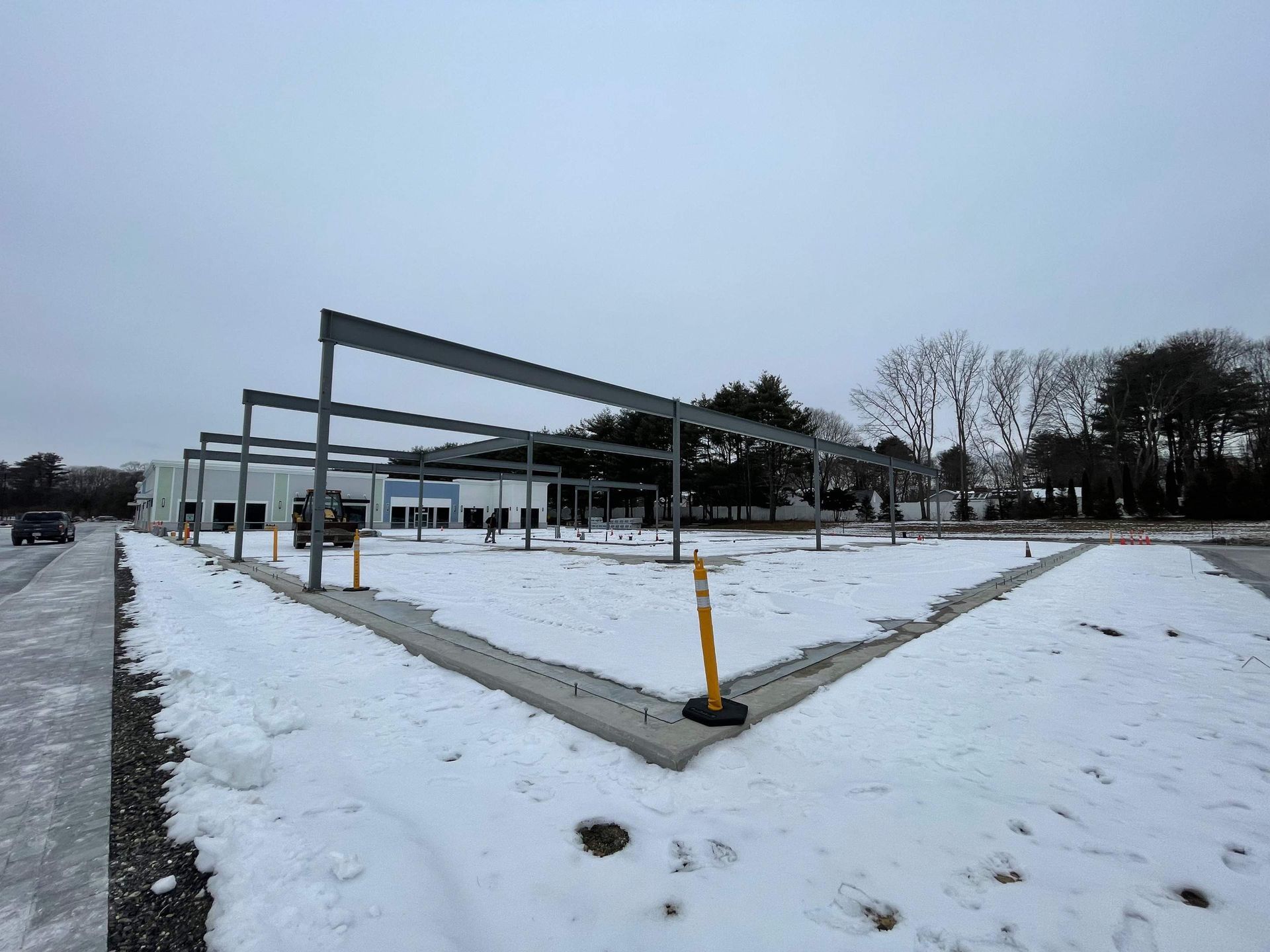 Steel frame of a building under construction, covered in snow. A cloudy sky is overhead.