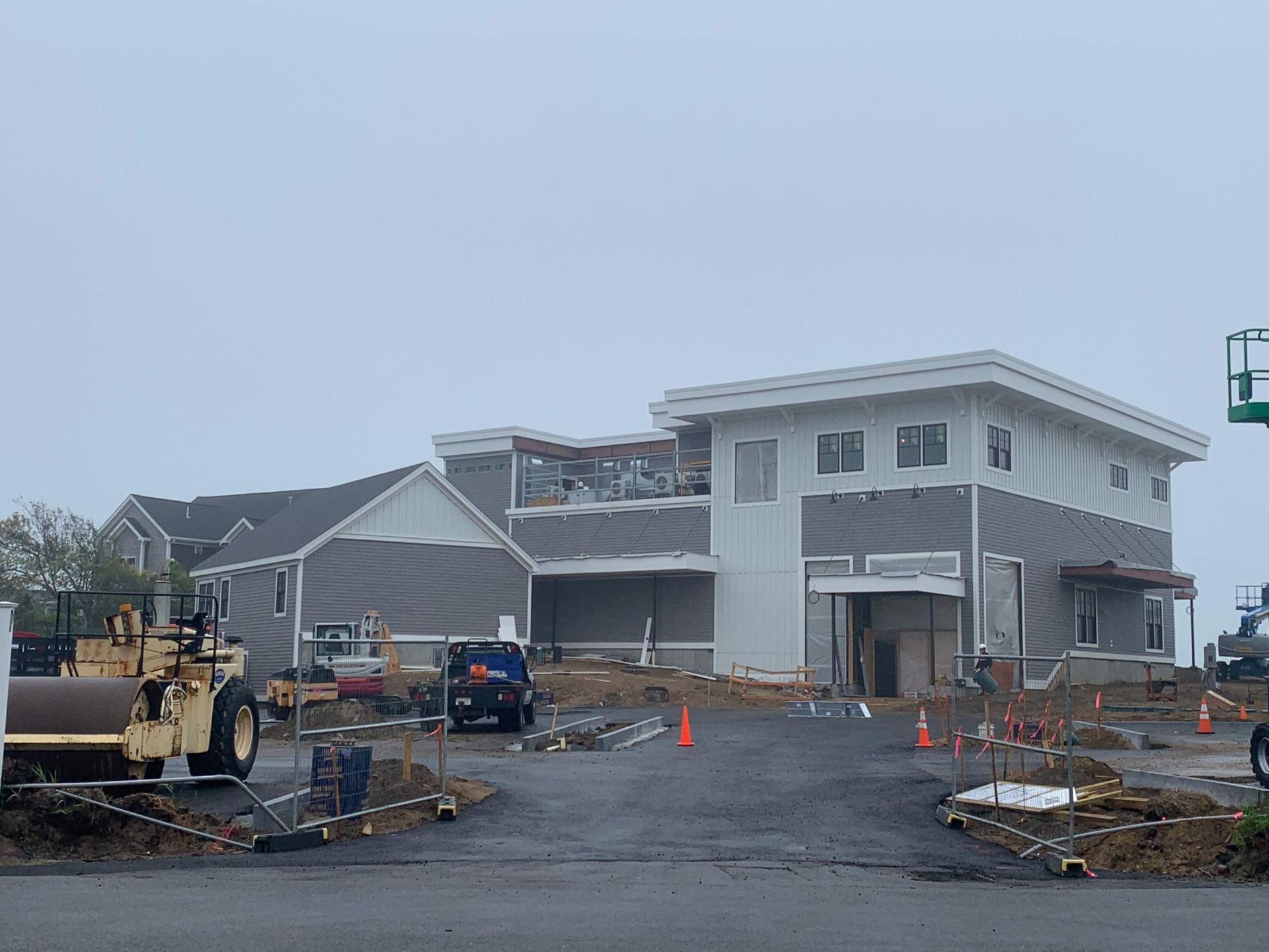 Construction site of a two-story building with gray siding; heavy machinery and gravel driveway.