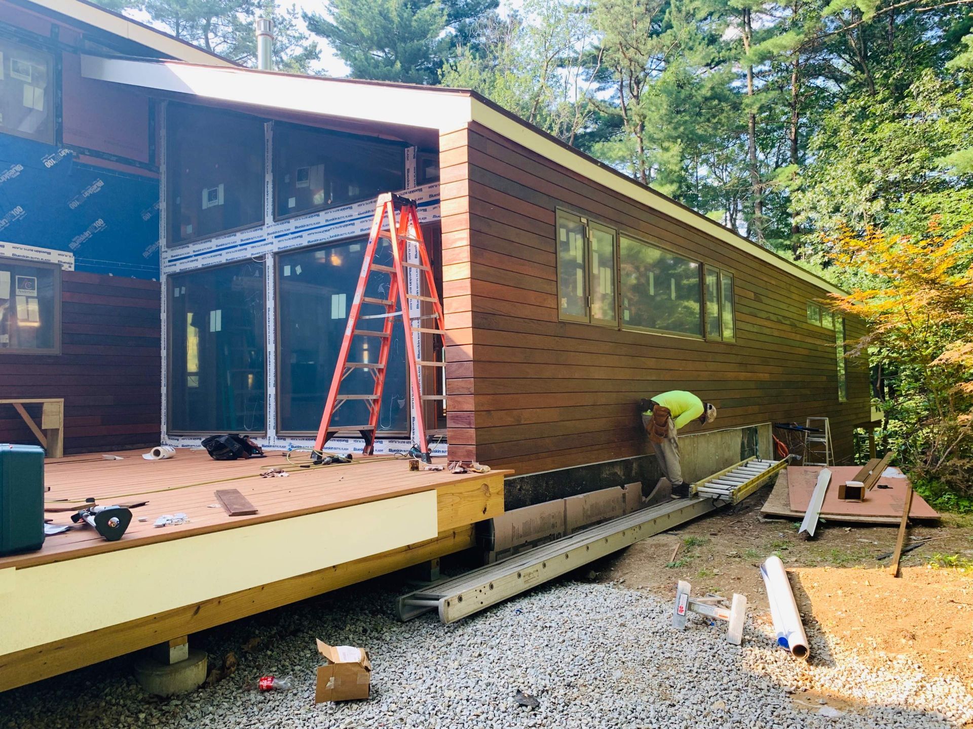 Exterior house renovation; worker installing brown siding, a ladder and deck.