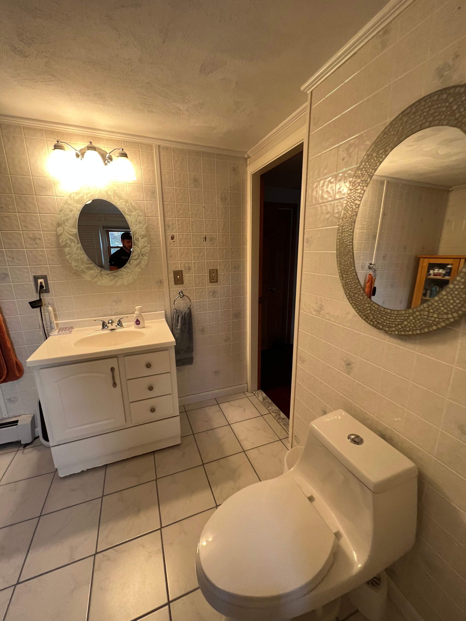 Bathroom with white tile, vanity, toilet, and two round mirrors.
