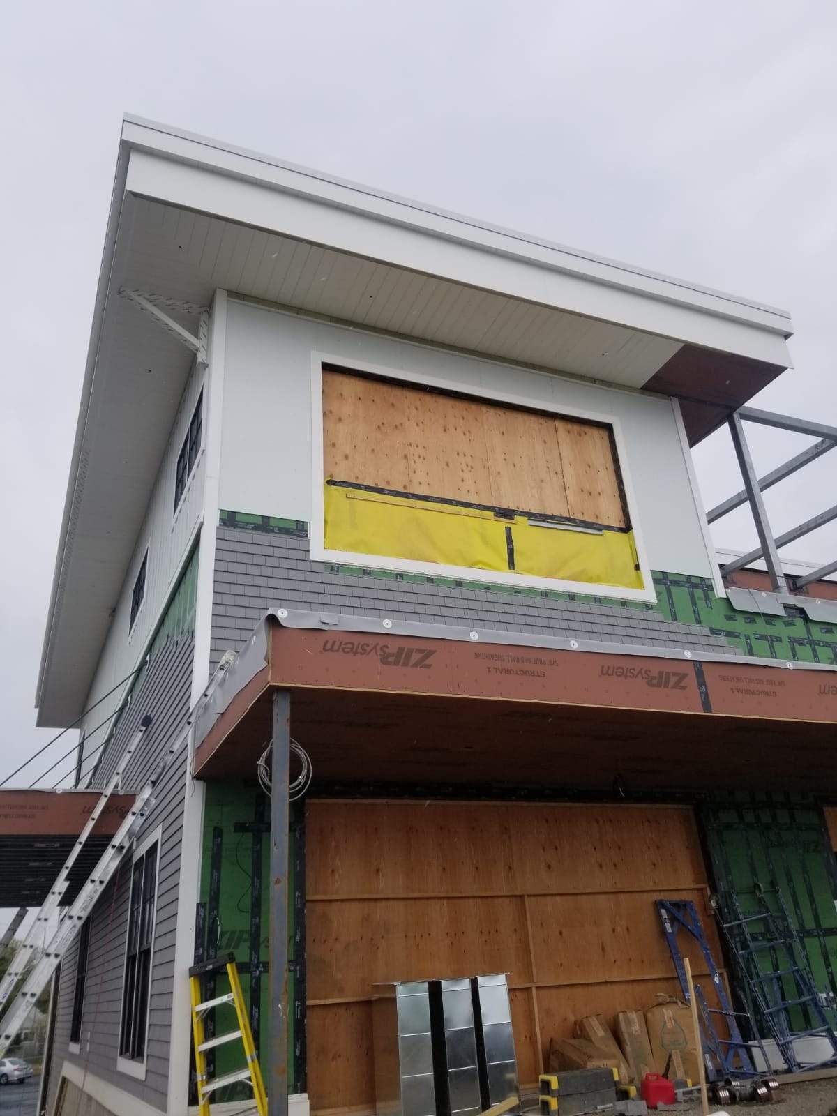 Building exterior under construction with plywood covering windows and gray siding.