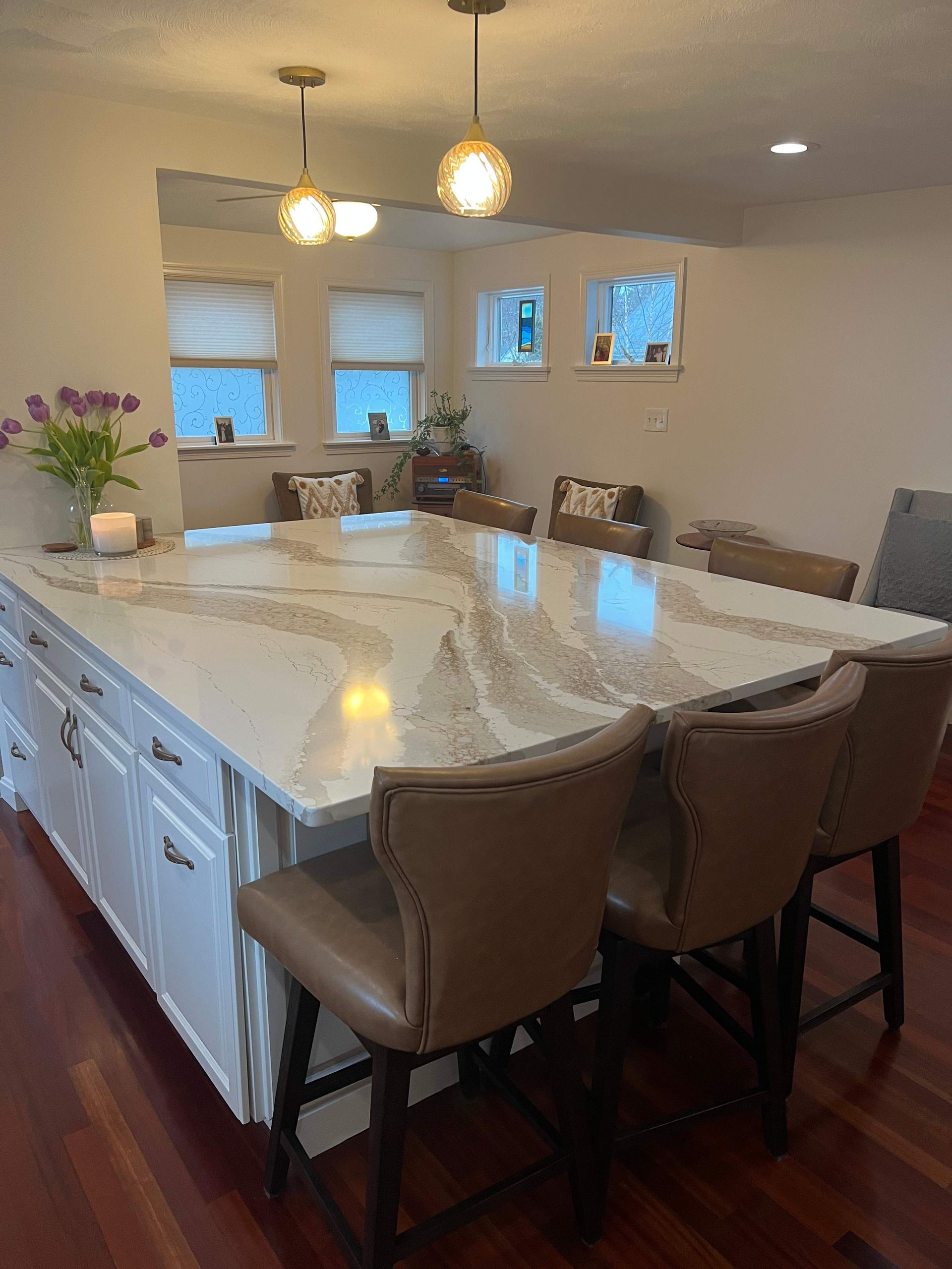 Kitchen with white island, stone countertop, brown leather bar stools, and pendant lights.