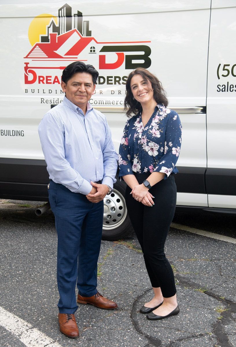 Two people stand in front of a van. Man in blue shirt, woman in floral shirt. Dream Builders logo visible.