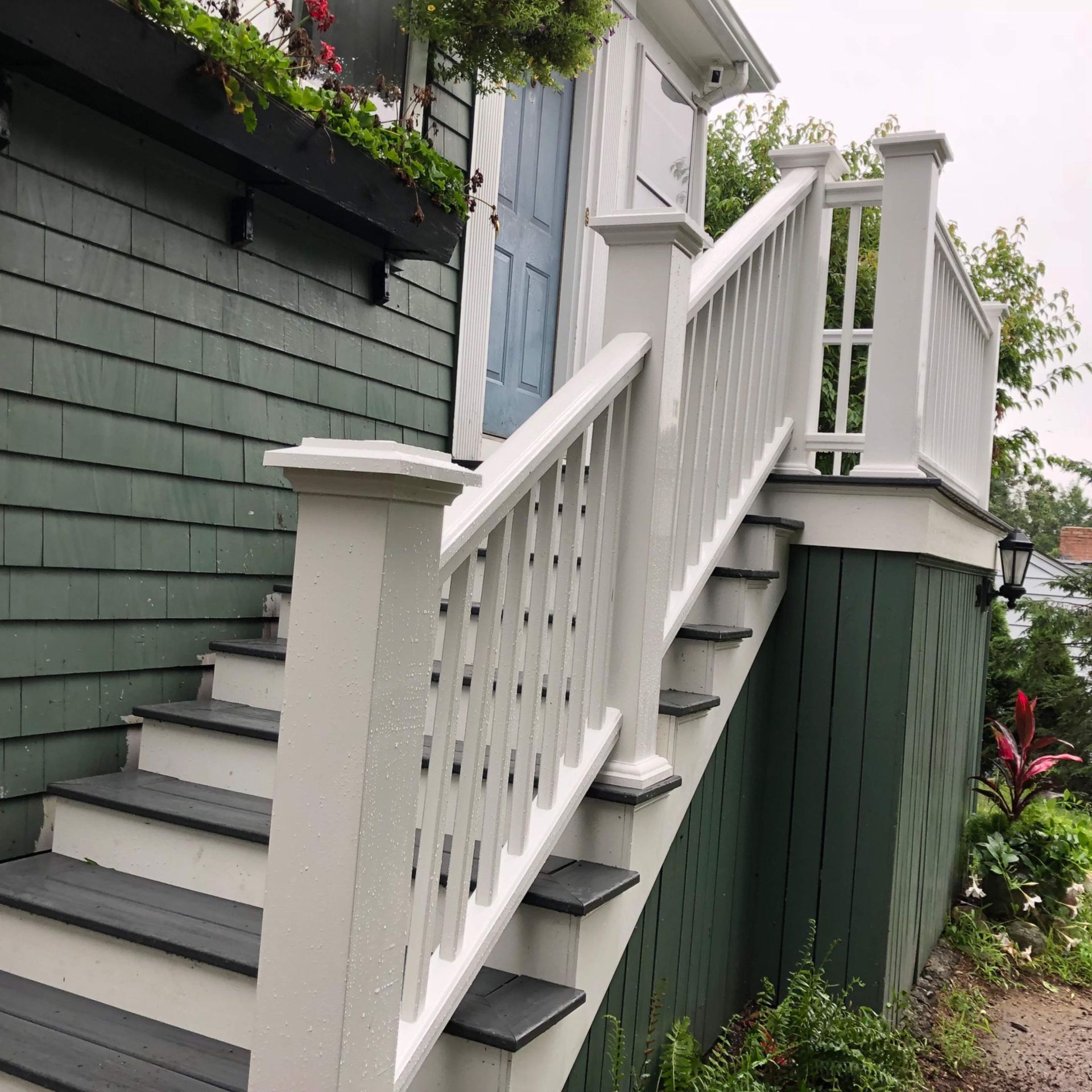 Exterior staircase with white railing leading to a light blue door. Green siding.