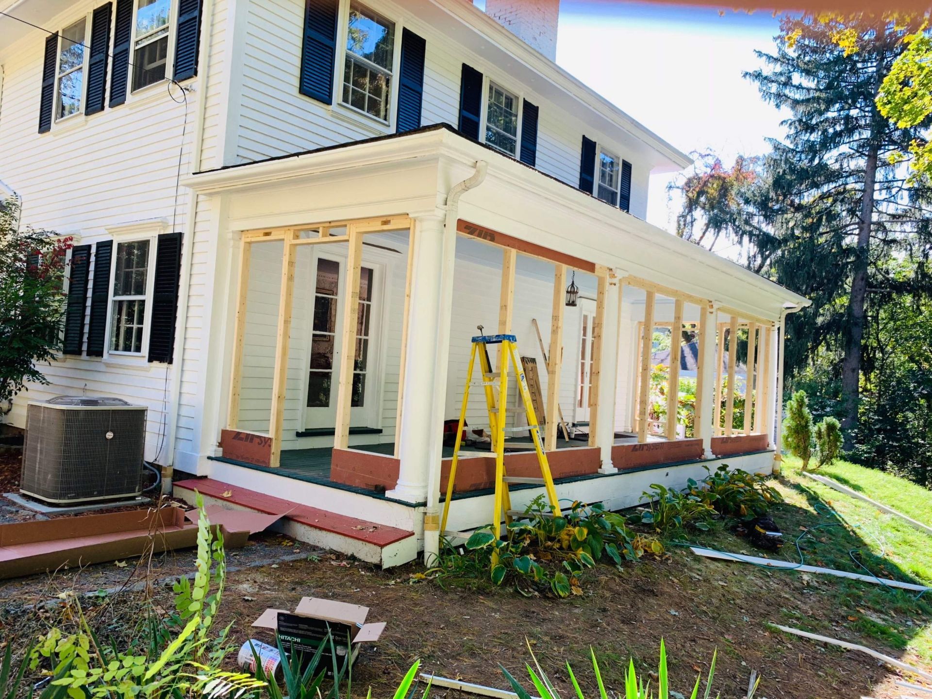 Renovation of a white two-story house porch. Wooden framing and a yellow ladder are visible.