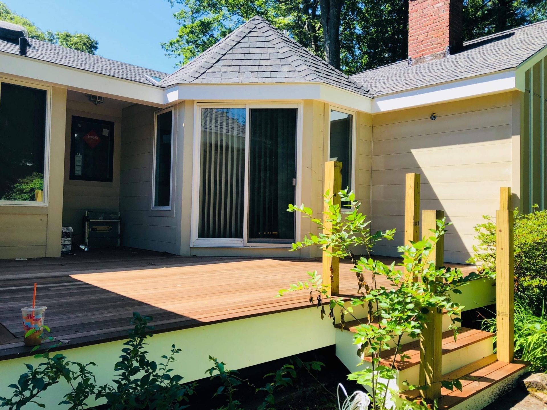 Wooden deck with steps, leading to a yellow house with a sliding glass door and a small, octagonal roof.
