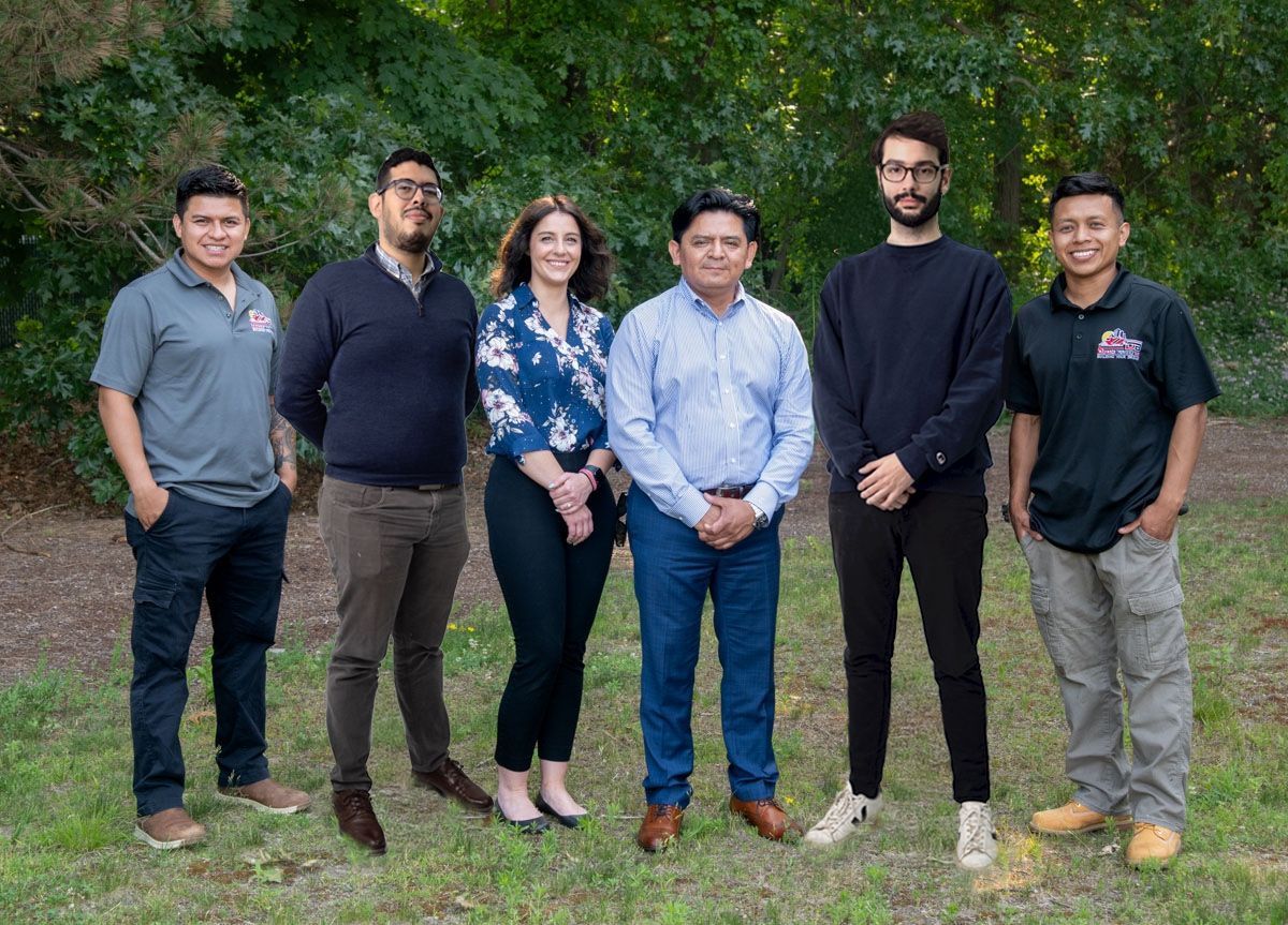 Group of six people standing in front of trees. They are wearing various outfits; some are smiling.