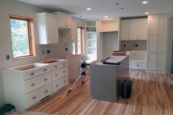 White kitchen cabinets under construction, light wood floors, and gray island.
