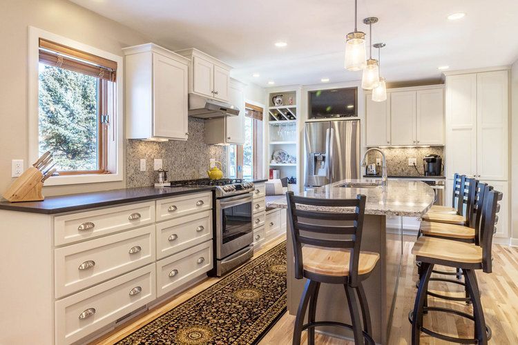 Bright kitchen with white cabinets, stainless steel appliances, and a granite island with bar stools.
