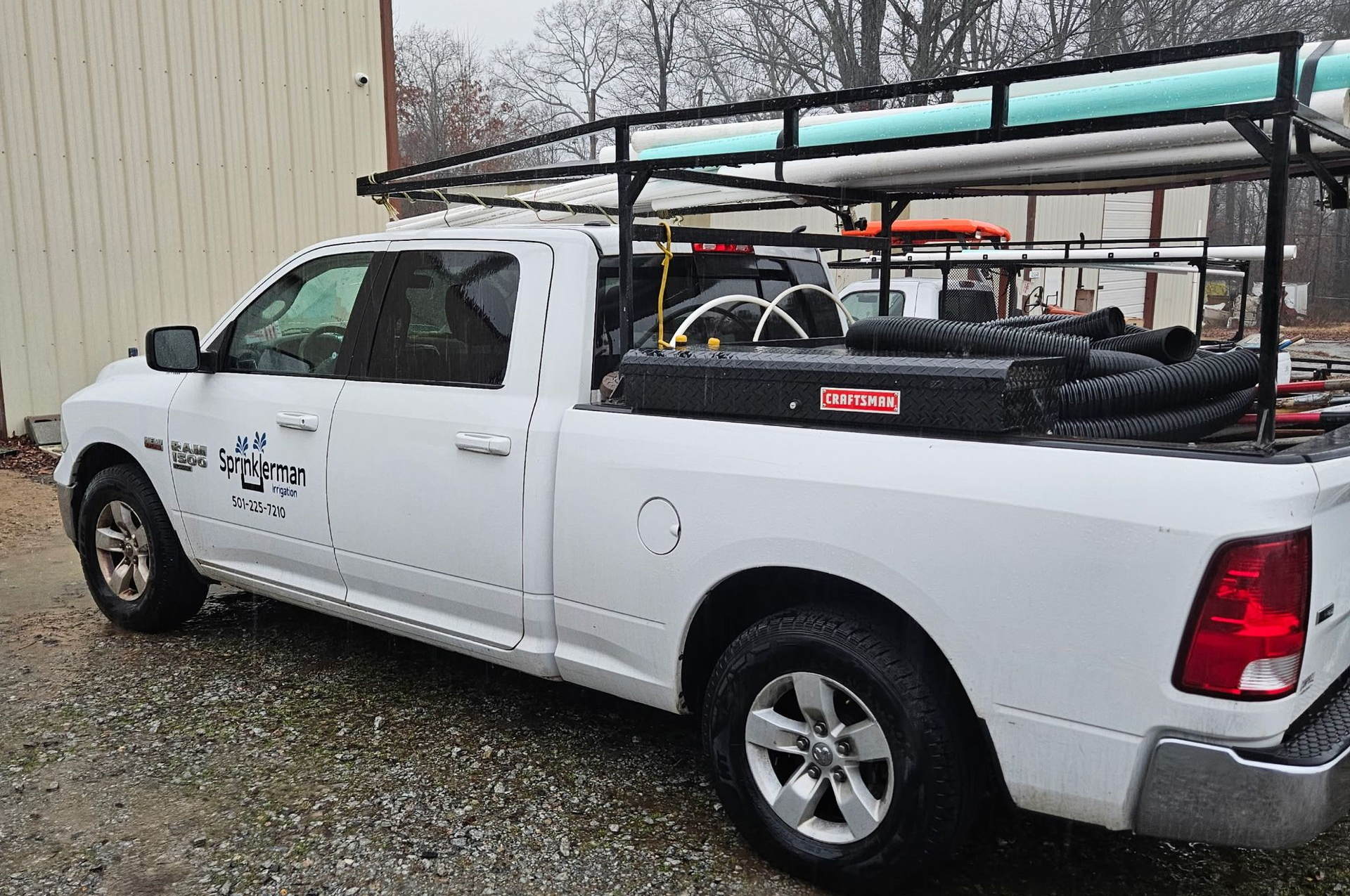 White pickup truck with a rack carrying pipes parked outside a building.