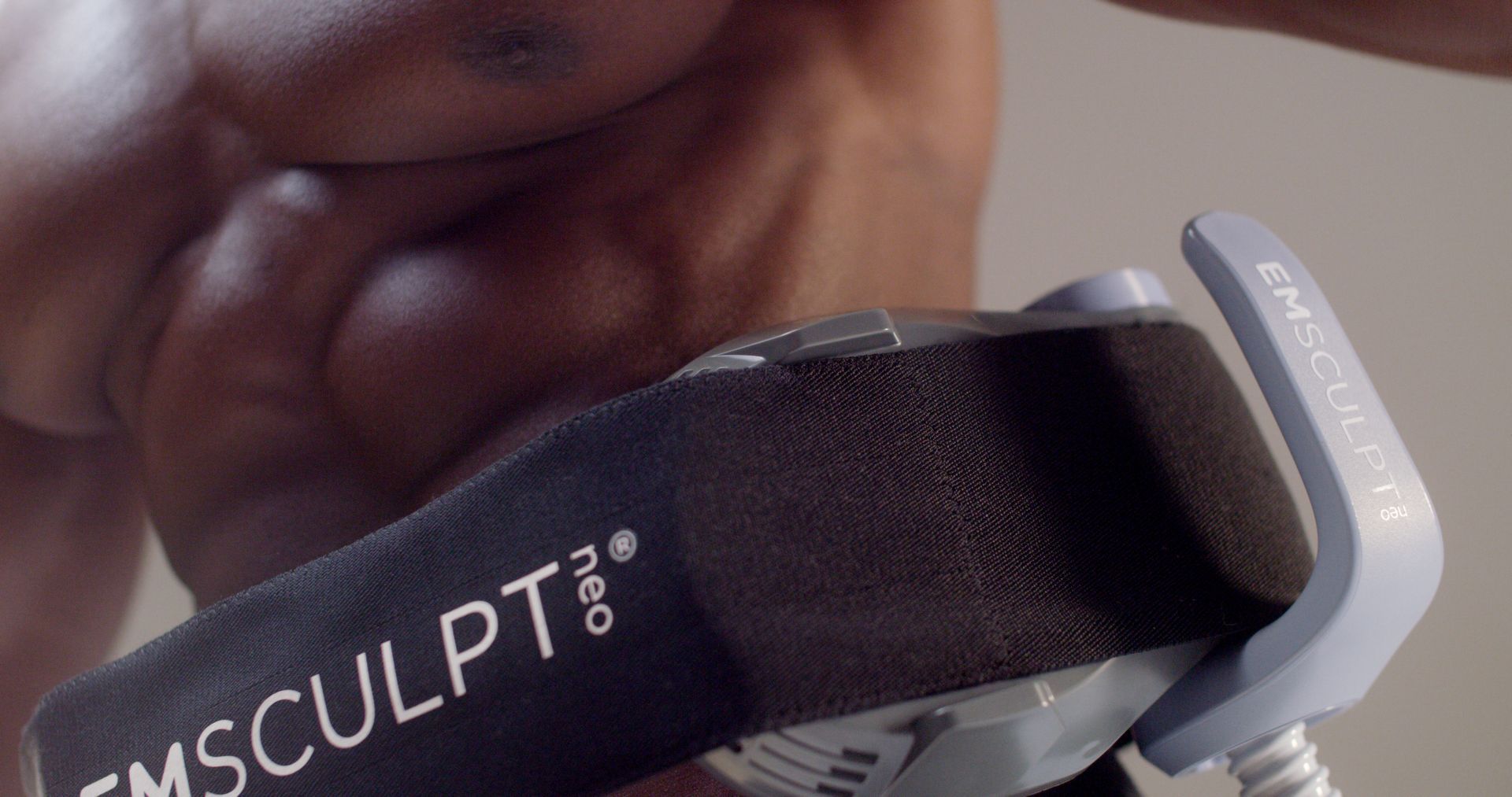 Close-up of a person using a black EMSculpt muscle-stimulation belt on the torso