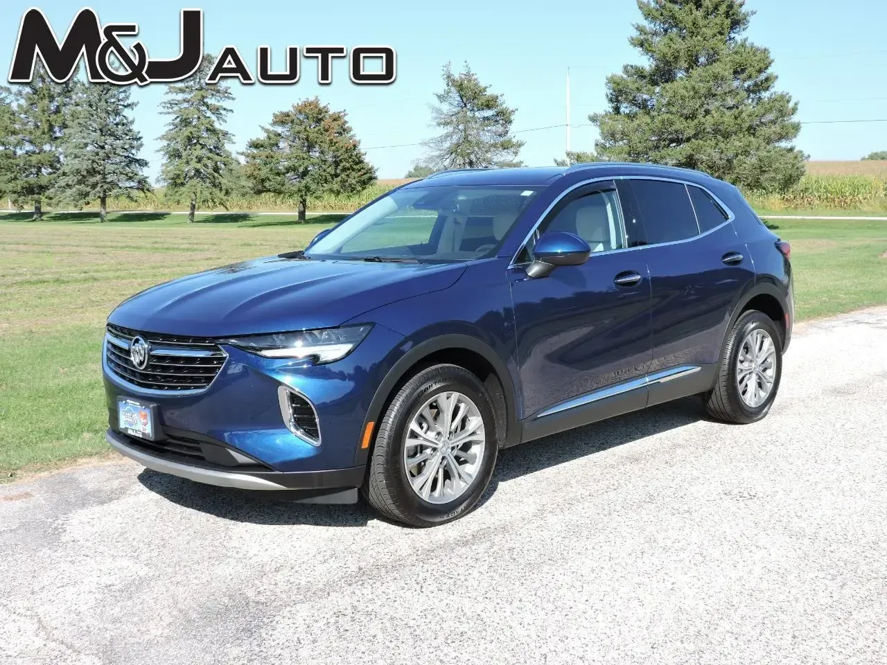 Blue SUV parked on a sunny roadside with a grassy field and trees in the background