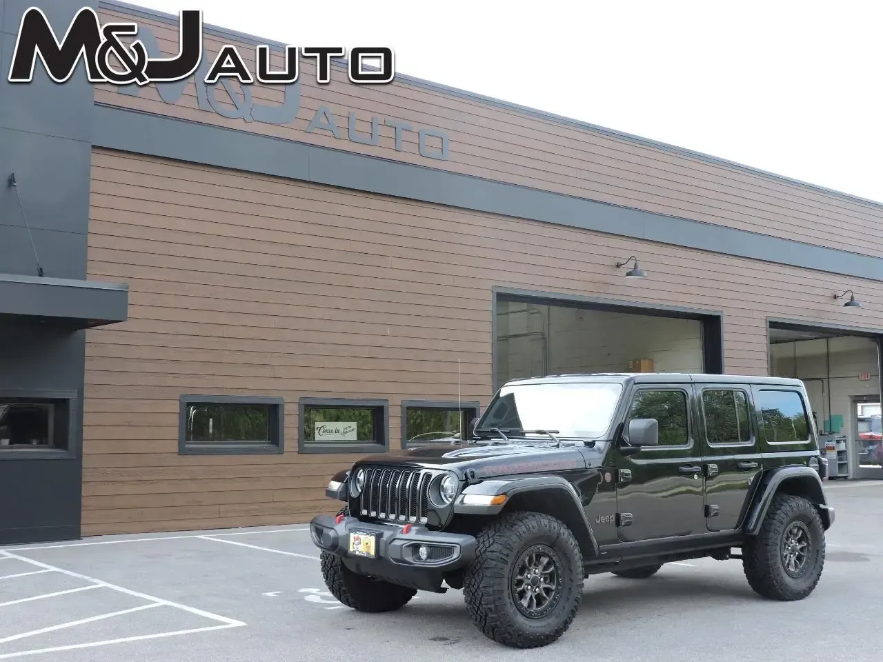 Black Jeep Wrangler parked outside M&J Auto shop with brick building in the background