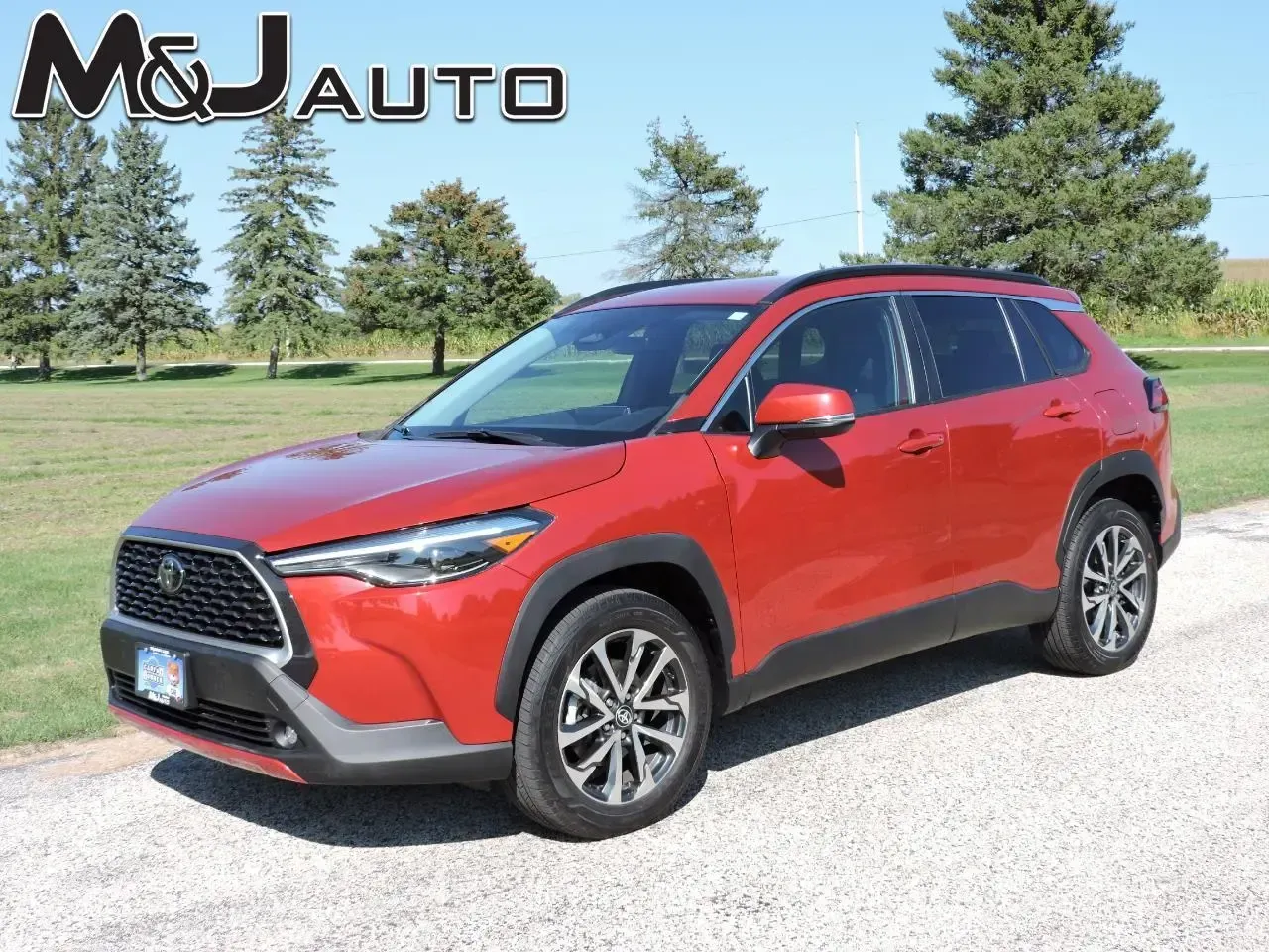Red SUV parked on a gravel lot with trees in the background, M&J Auto logo in the corner
