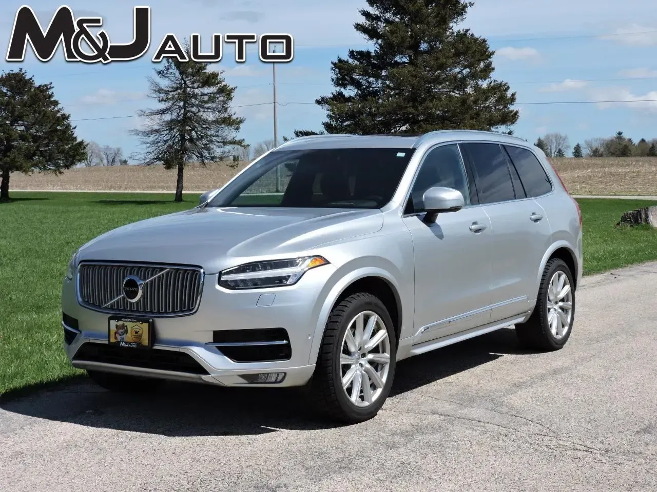 Silver Volvo SUV parked on a roadside beside grass and trees under a blue sky