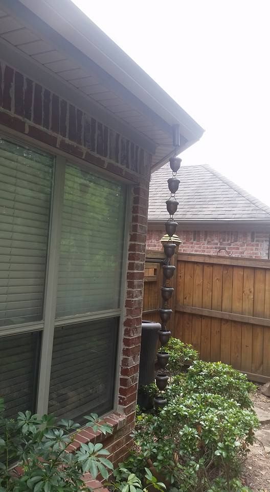 A rain chain is attached to the side of a brick house.