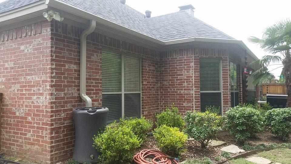 A brick house with a gutter and a hose in front of it.