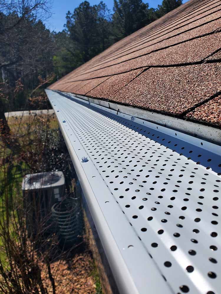 A gutter with holes in it is on the roof of a house.