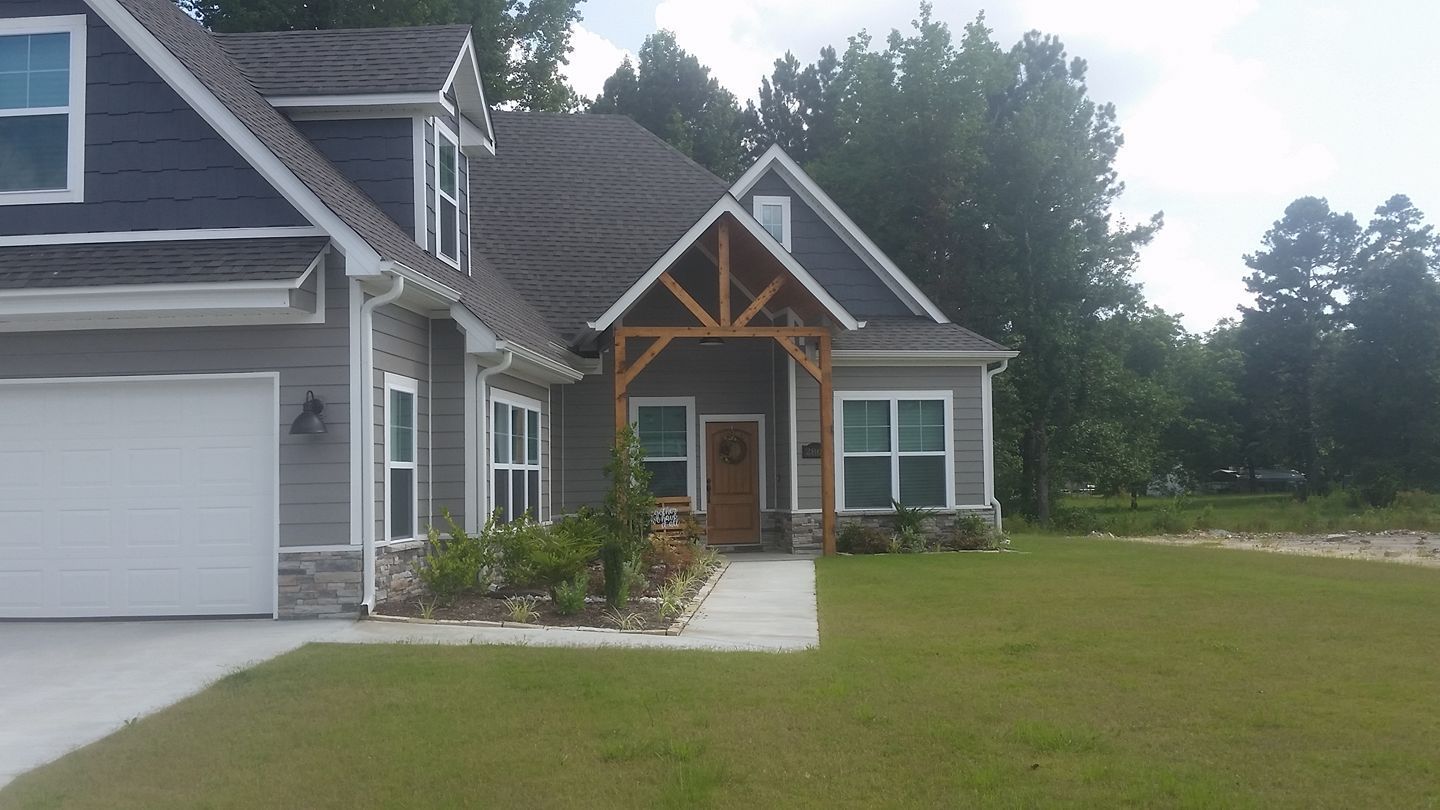 A large gray house with a white garage door is sitting on top of a lush green field.