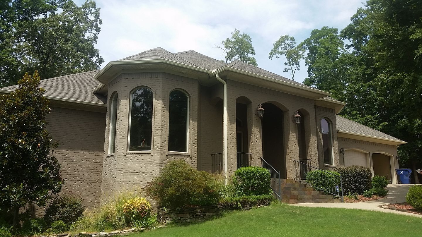 A large brick house with arched windows is surrounded by trees