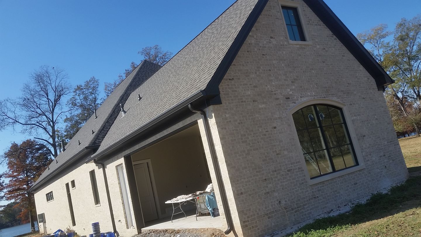 A small white house with a black roof is sitting on top of a lush green field.
