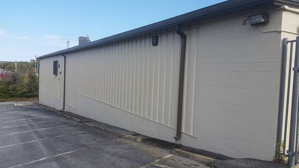 A large white building with a black roof is sitting next to a parking lot.