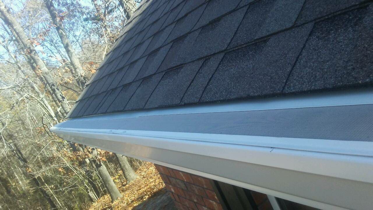 A close up of a gutter on a roof with trees in the background.