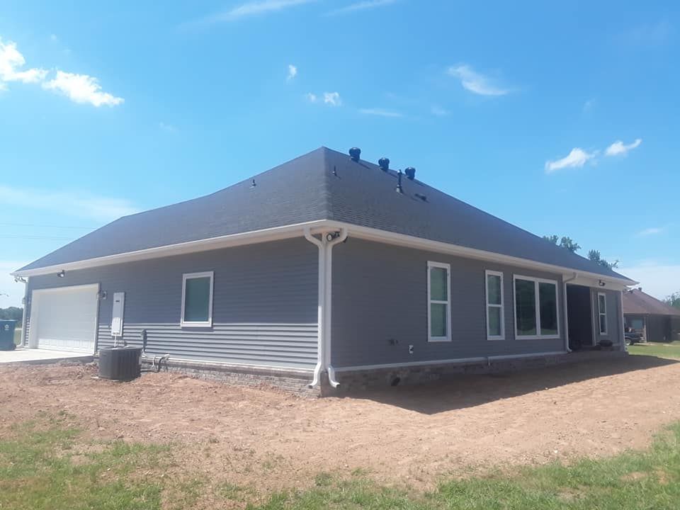 A gray house with a black roof is sitting on top of a dirt field.